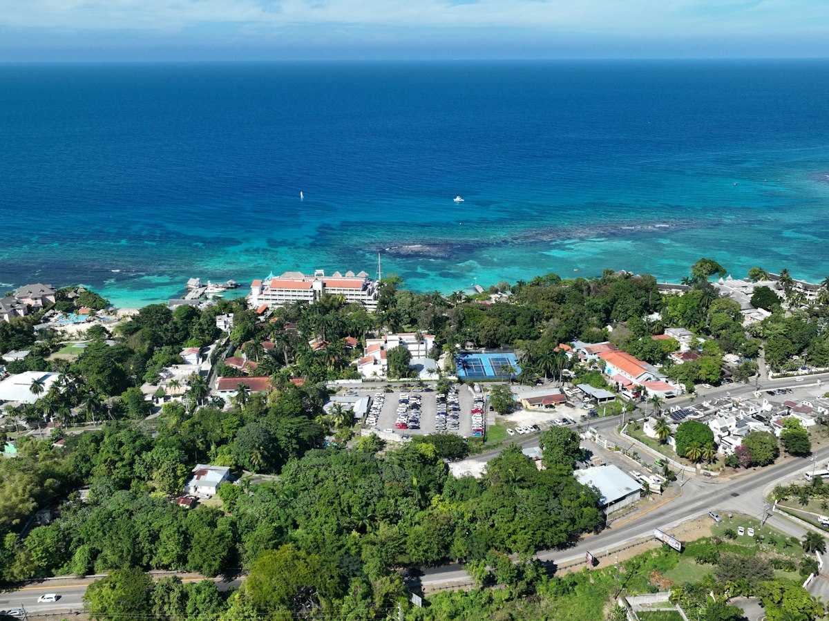 Aerial view of a Jamaican coastal resort strip in Montego Bay with hotels, a pier, tennis court and coastline, no people visible