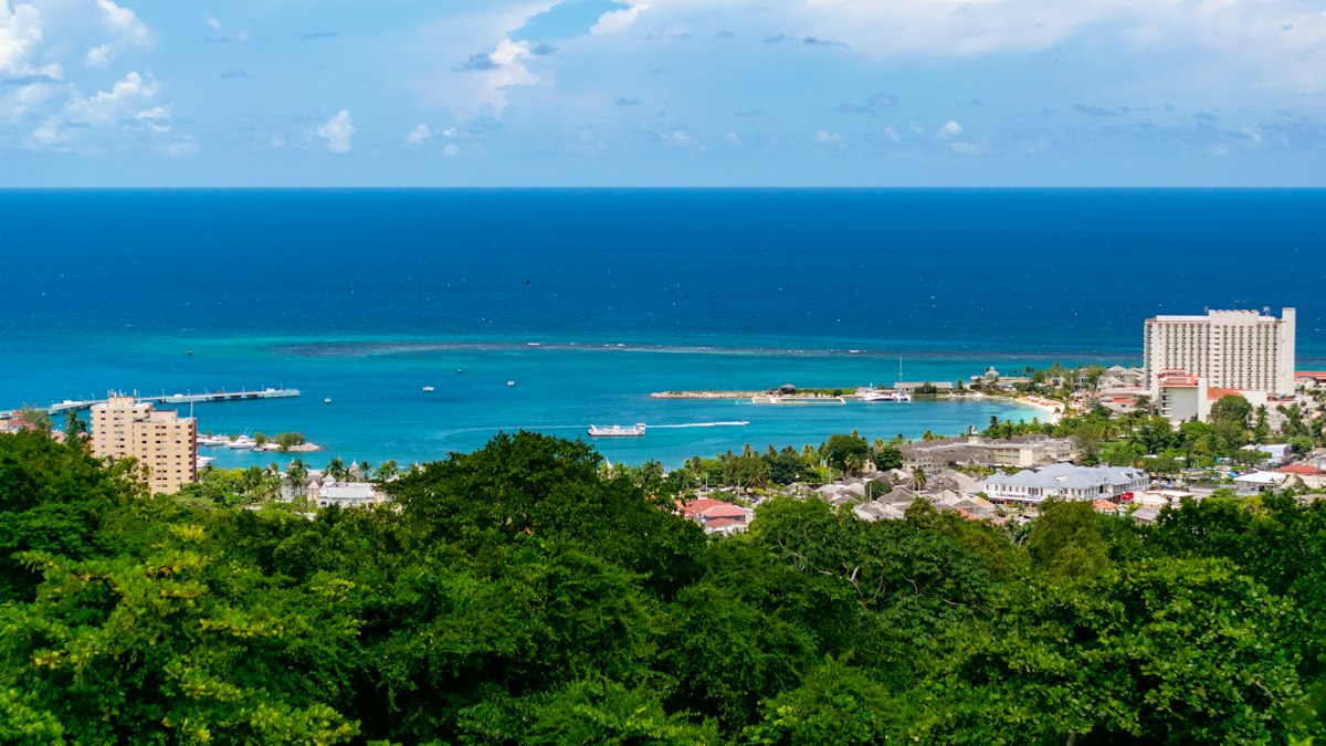 Aerial hillside view over a Jamaican north coast bay, hotel tower and pier along the turquoise water, no people visible